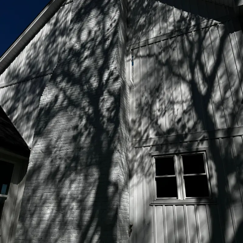 A low angle shot of a white house with a dark blue sky. The house features vertical siding and a brick chimney, all painted white