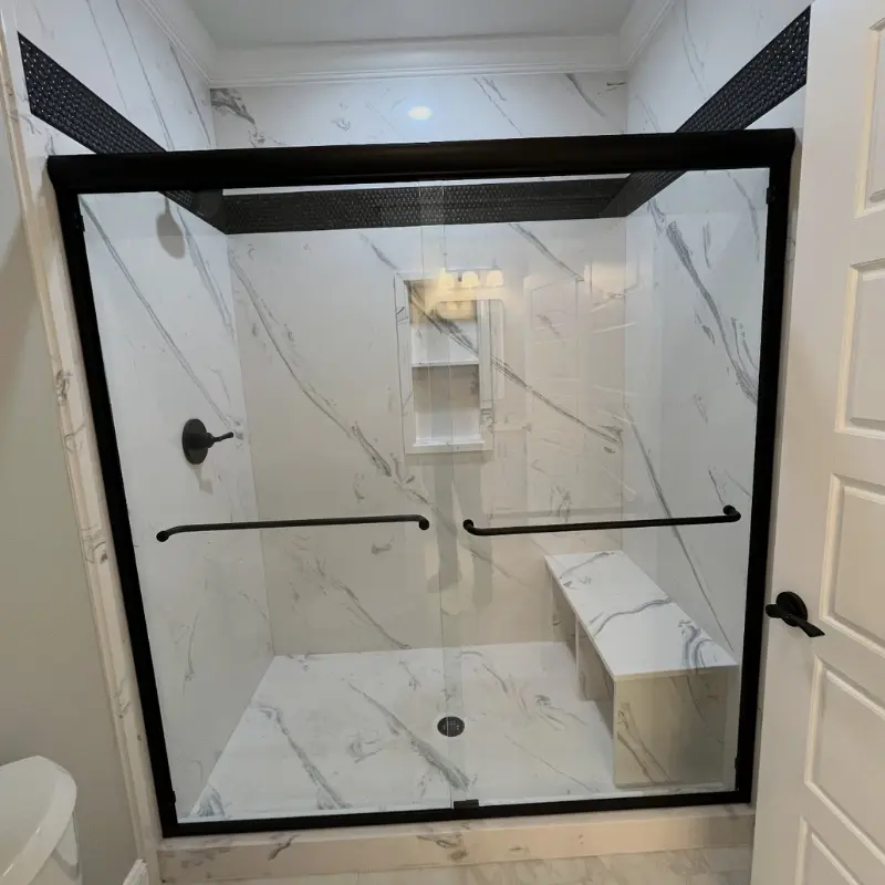 A luxurious bathroom features a spacious shower with black framed glass doors, white marble walls and floor, and a built in bench.
